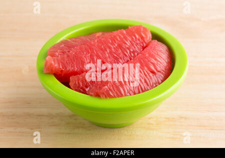 Sections of red grapefruit in a green bowl on a wood table top. Stock Photo