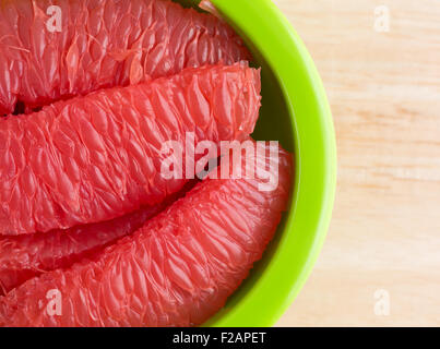 Top close view of sections of red grapefruit in a green bowl on a wood table top. Stock Photo