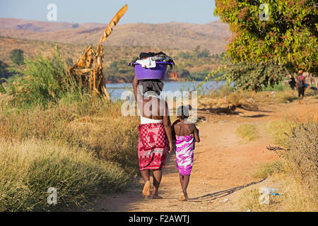 Malagasy daughter and mother with laundry basket on head while walking along Tsiribihina river, Miandrivazo, Menabe, Madagascar Stock Photo