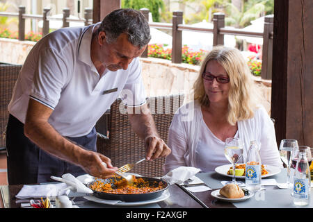 Spanish waiter serving paella to Female diner / tourist. Fuerteventura, Canary Islands. Stock Photo