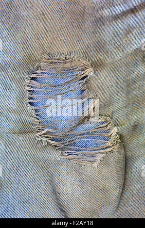 Close view of a ragged hole in muddy worn blue jeans. Stock Photo
