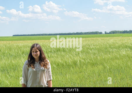 Young seventeen year old girl standing on a background of green field on a summer day. Stock Photo