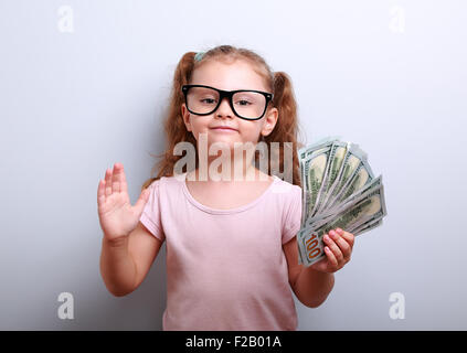 Happy business kid girl holding money and explaining something on blue background Stock Photo