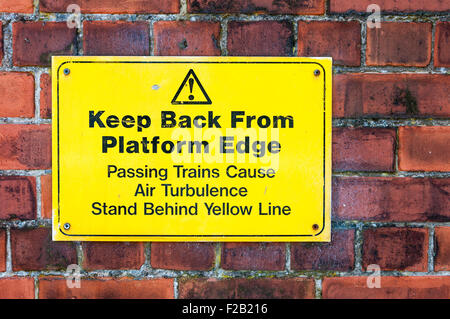 Sign at a railway platform warning passengers to keep back from the edge and to stand behind yellow line. Stock Photo