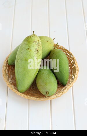 Green mangoes in bamboo basket on white timber