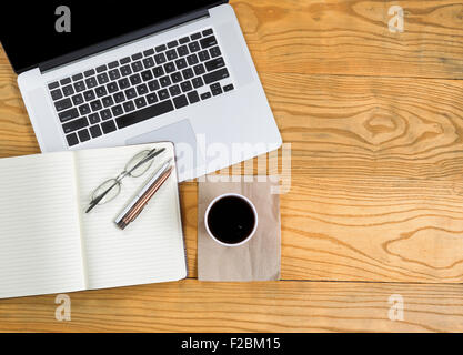 Top view of computer laptop with dark coffee, notepad, reading glasses and pens on desktop. Stock Photo