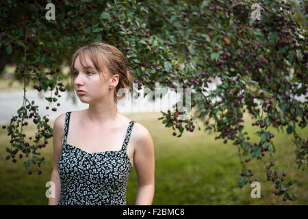 Portrait of young woman wearing summer dress outside under crabapple tree looking away with copy space Stock Photo