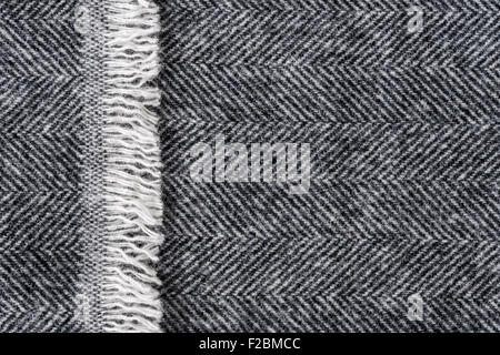 Herringbone wool tweed fabric background with closeup on textile texture and overlapping fringe edge Stock Photo