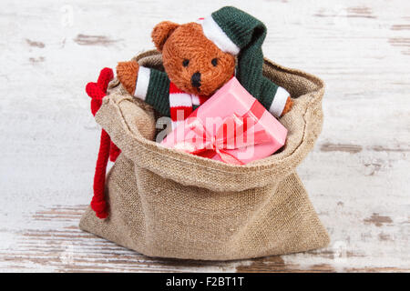 Teddy bear and wrapped colorful gifts for Christmas, birthday, valentines or other celebration in jute bag on old wooden white t Stock Photo