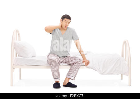 Studio shot of a young man in pajamas waking up with a neck pain isolated on white background Stock Photo