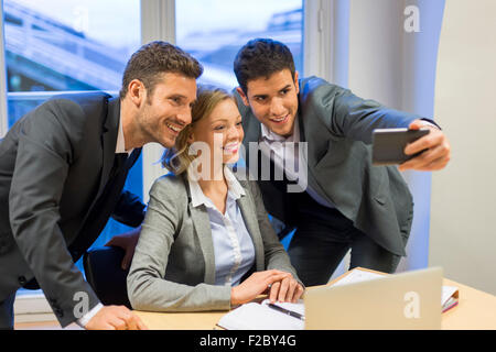 Portrait of three smiling business people taking a selfie with smartphone Stock Photo