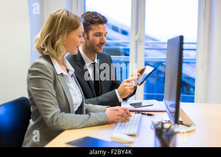 two colleagues in office using computer and consulting cellpone Stock Photo
