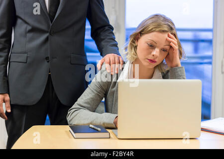 depressed businesswoman using laptop in her office with colleague Stock Photo