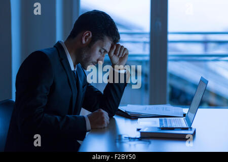 Pensive businessman sitting in darkness office, fist on forehead Stock Photo
