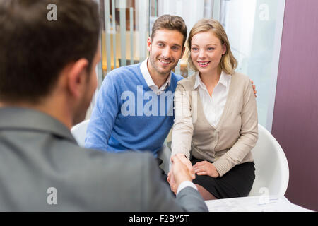 Businessman shaking hands with couple in office Stock Photo