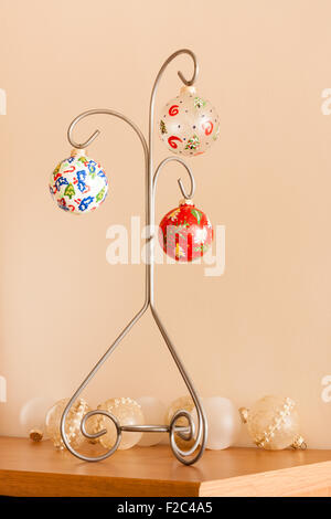 Hand painted Christmas ornaments hung on a decorative frame. A few retro and plain ornaments are also on the table. Stock Photo
