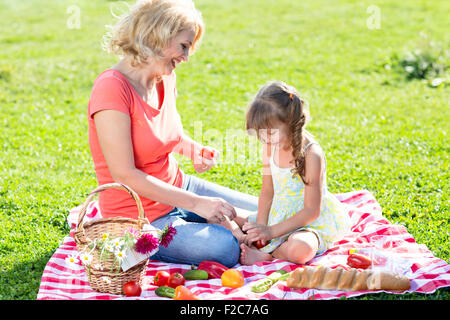 beautiful middle-aged mother and daughter having picnic in the park on a sunny day Stock Photo