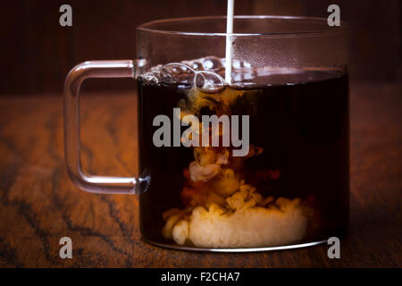 Cream being poured into coffee in glass mug Stock Photo