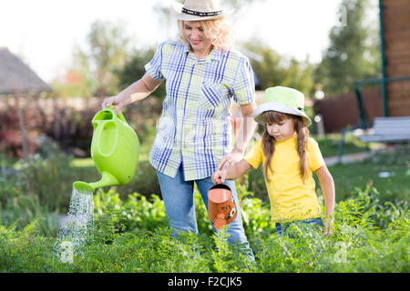 Mother And daughter watering plants in garden. Stock Photo