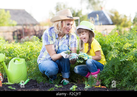 Mother and little girl planting strawberry seedlings in summer time