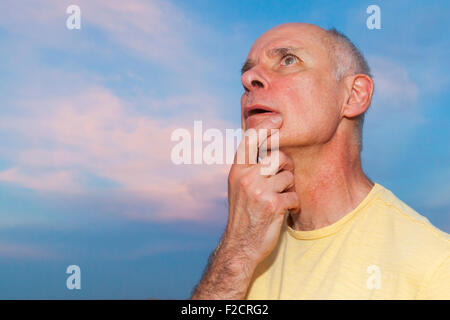 A senior man posing with thoughtful, serious and silly expressions outdoors against a blue sky. Stock Photo