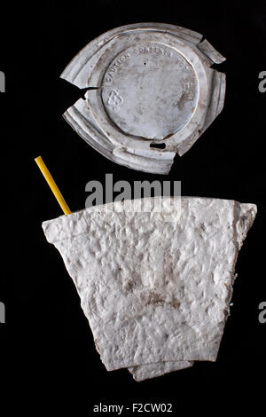 Flattened dirty styrofoam  coffee cup with yellow coffee stirrer and dirty plastic cover on black background Stock Photo