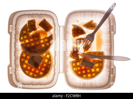 Looking straight down on waffles with butter and syrup in a plastic container with a fork and knife, half-eaten Stock Photo