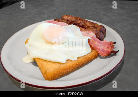 Breakfast composed of a fried egg, two sausages, one piece of bacon and a slice of fried bread on a plate. Stock Photo
