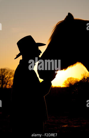 Horse and his cowboy silhouetted against a sunset, head to head Stock Photo