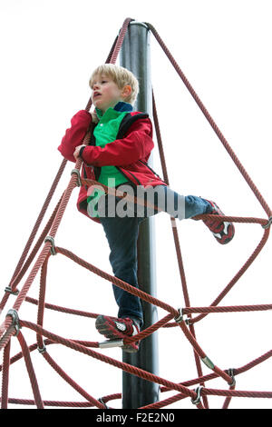 blond boy climbing on ropes on playground on a rainy day Stock Photo