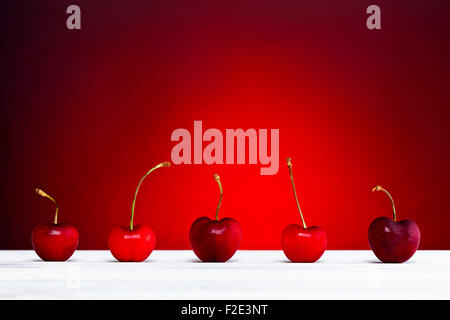 Row of freshly cherries on white wooden table over red background. Stock Photo