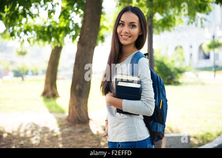 Portrait of a beautiful smiling student standing outdoors with books Stock Photo