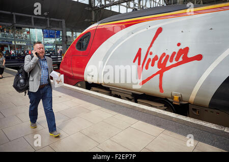 Manchester Piccadilly railway station Virgin logo on a Pendolino train from London   Passengers passing blurred walking to   Man Stock Photo