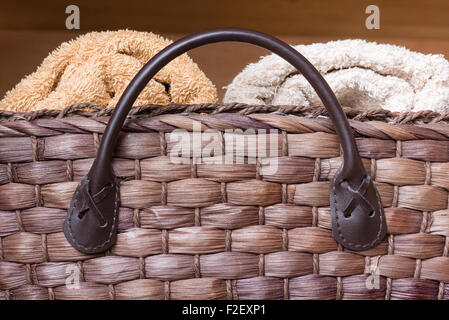 A close up shot of a brown woven wicker basket with a light and dark tan rolled towel in it. Stock Photo