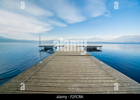 Prospectic view from a wooden jetty, calm lake water, horizon and mountains in the background Stock Photo