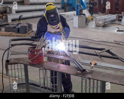 Welder with protective gear welding a metal, industrial staircase at a workshop in Thailand. Stock Photo