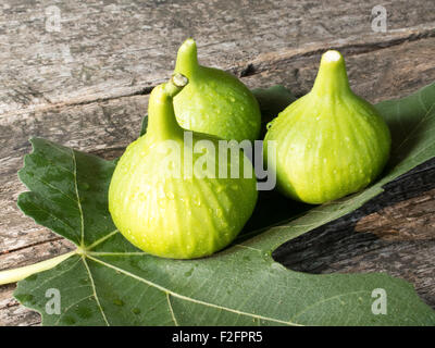 Three fresh figs on a fig leaf on a wooden surface Stock Photo