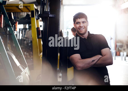 Portrait confident mechanic leaning on forklift in auto repair shop Stock Photo