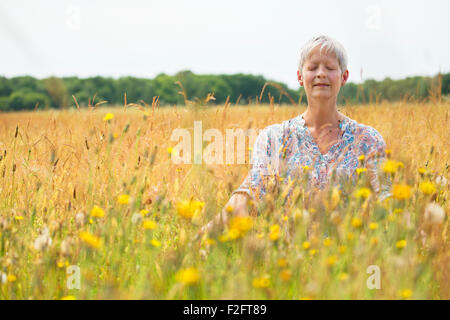 Senior woman meditating in rural field Stock Photo