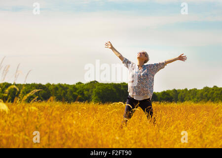 Exuberant senior woman with arms outstretched in sunny rural field Stock Photo