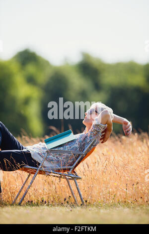 Carefree senior woman relaxing with book in sunny field Stock Photo