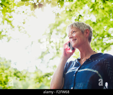 Smiling senior woman talking on cell phone below trees Stock Photo