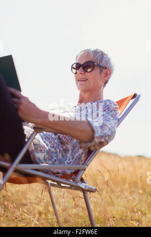 Senior woman reading book in sunny field Stock Photo