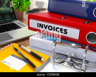 Red Ring Binder with Inscription Invoices on Background of Working Table with Office Supplies, Laptop, Reports. Toned Illustrati Stock Photo