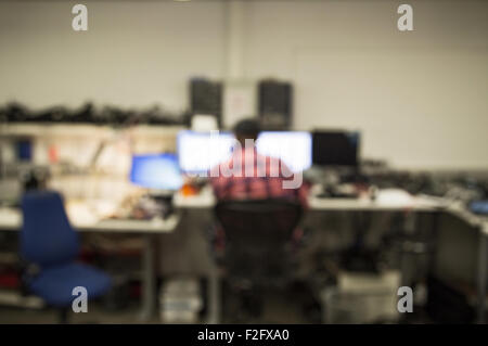 Out of focus shot of a man working in a computer repair center, computer parts and screens all around him Stock Photo