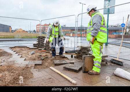 Workers laying paving slabs and truncated dome paving tiles to produce a tactile pavement to aid the visually impaired. Nottingham, England, UK Stock Photo