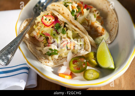 looking down at two fish tacos with spicy pickled cabbage, avocado and aioli on a plate with a fork and napkin Stock Photo