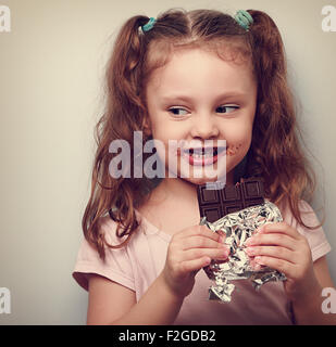 Curious cute kid girl eating dark chocolate and looking fun. Closeup vintage portrait Stock Photo