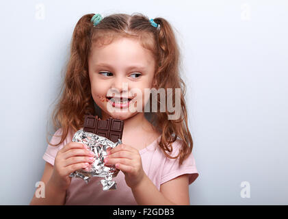 Curious cute kid girl eating dark chocolate and looking fun. Closeup portrait Stock Photo