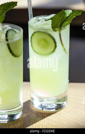 two cocktails in the sun in tall glasses garnished with mint and cucumber Stock Photo